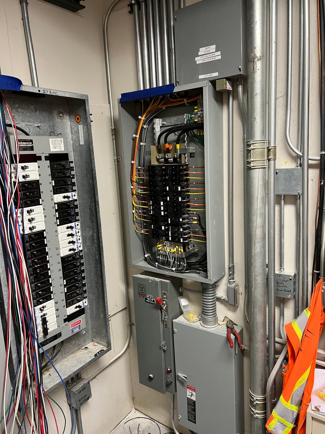 Electrical panel with circuit breakers and wiring in a utility room. Safety gear visible.