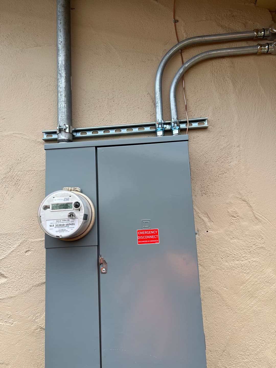 Gray electrical meter box with emergency disconnect warning sign on a wall.