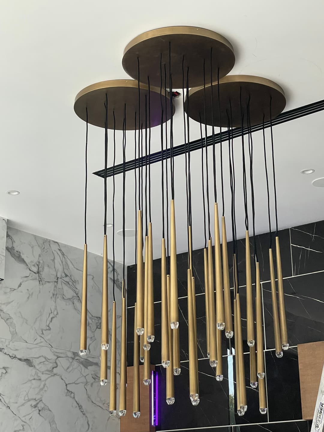 Modern gold chandelier with hanging cylindrical lights in a sleek interior setting.