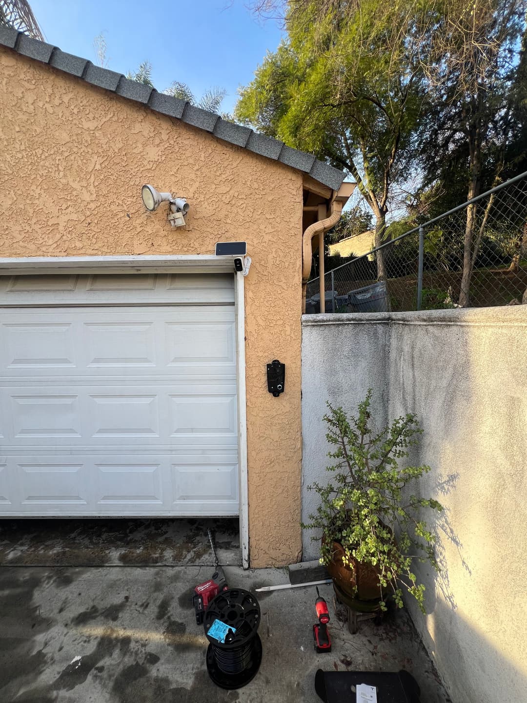 Garage wall with a security camera, potted plant, and tools on the concrete floor.