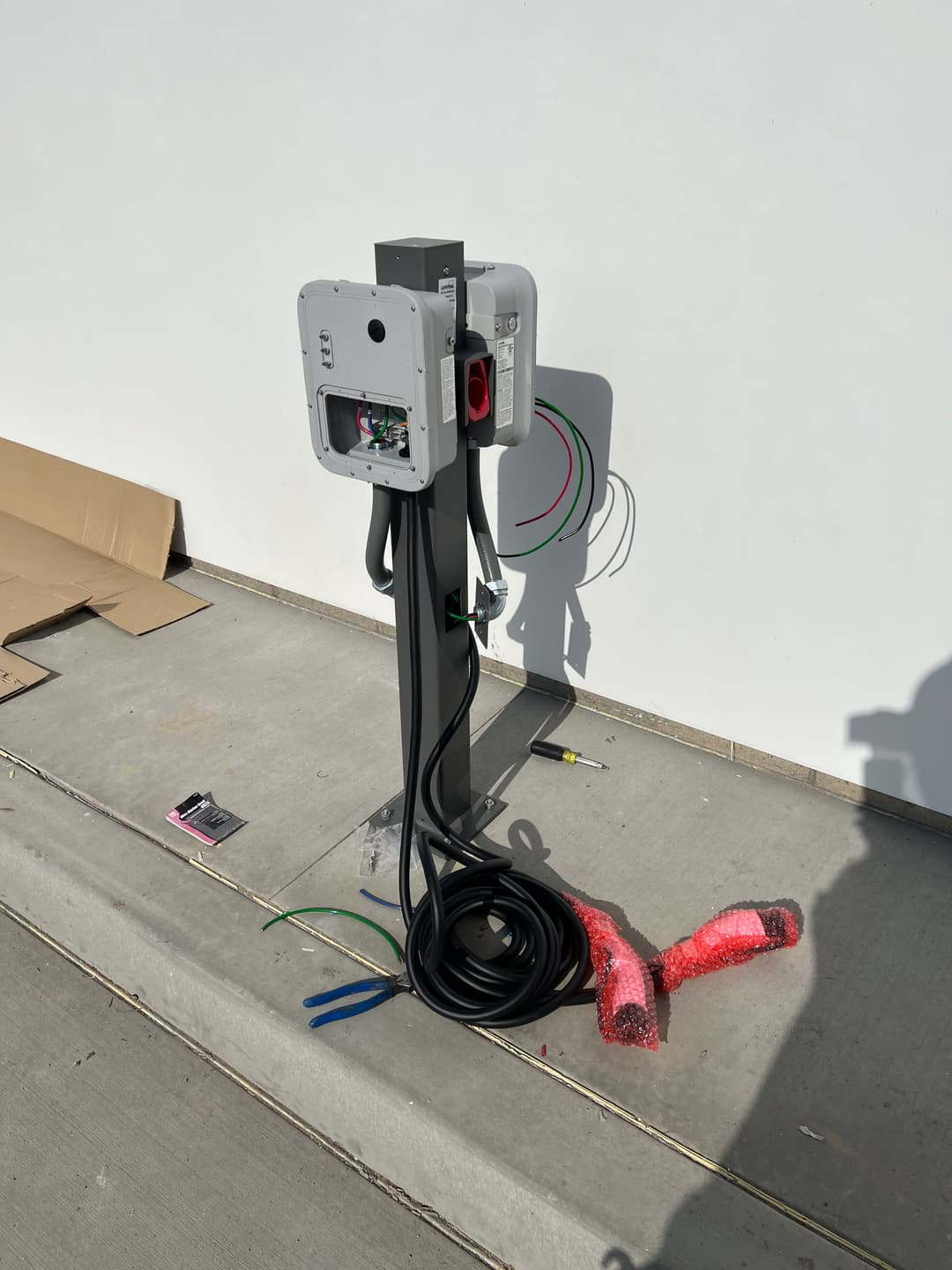 Electric vehicle charging station on a concrete surface, surrounded by packaging materials.