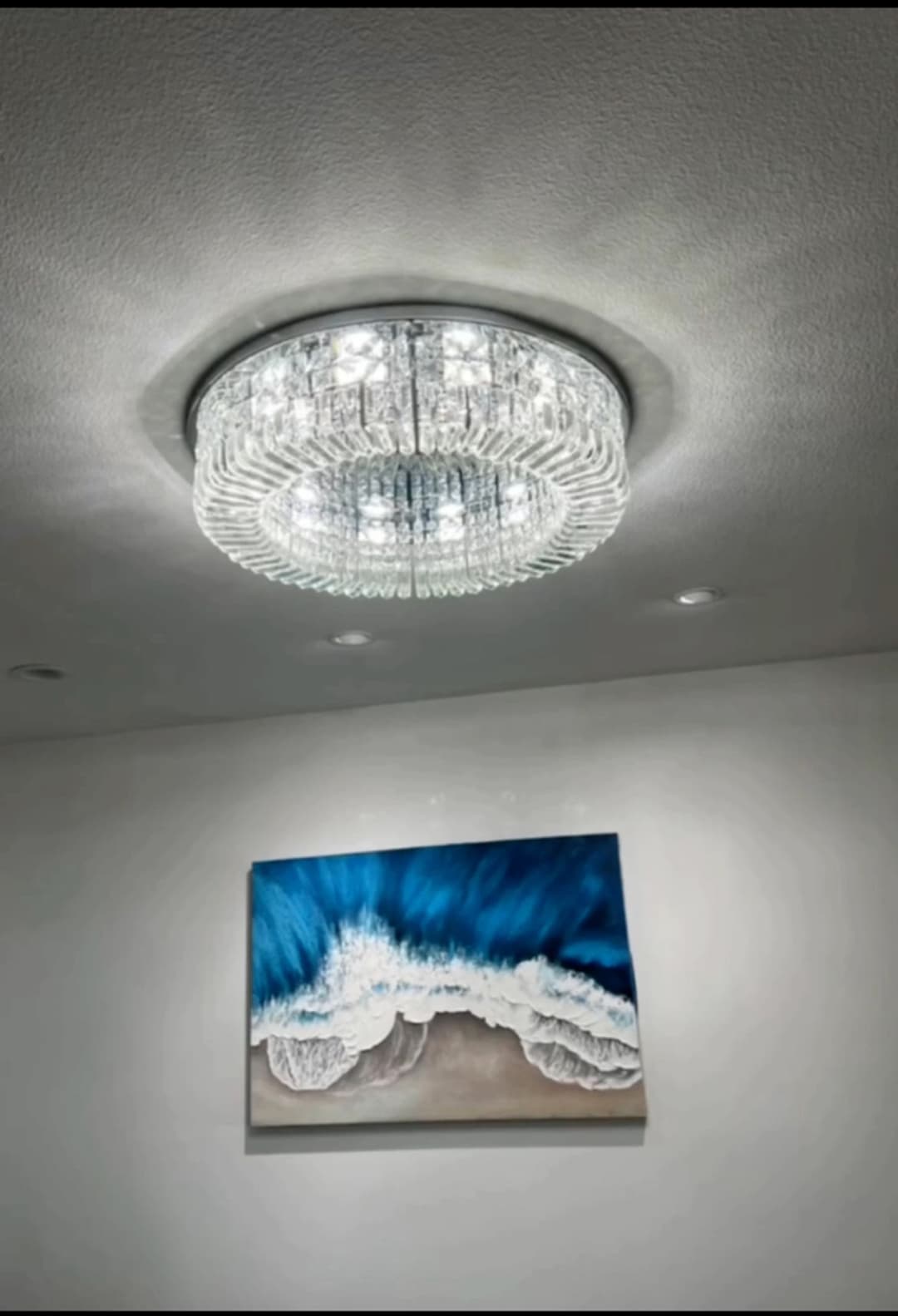 Elegant crystal chandelier above a coastal-themed artwork with waves and sandy shore.