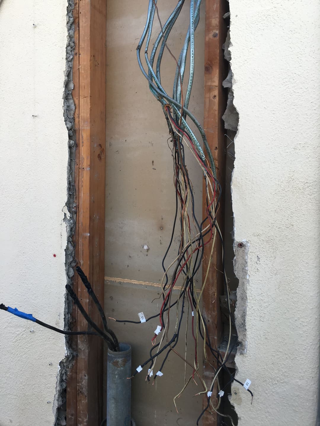 Exposed electrical wires and plumbing inside a wall during renovation.