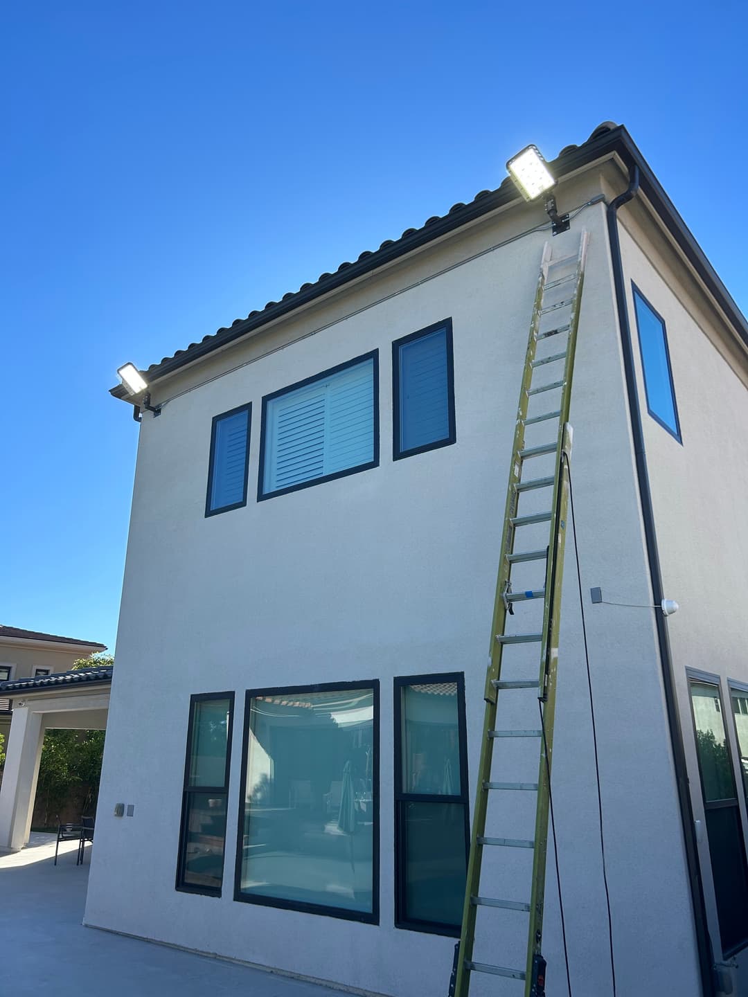 Two floodlights mounted on a modern house with a ladder leaning against the wall.