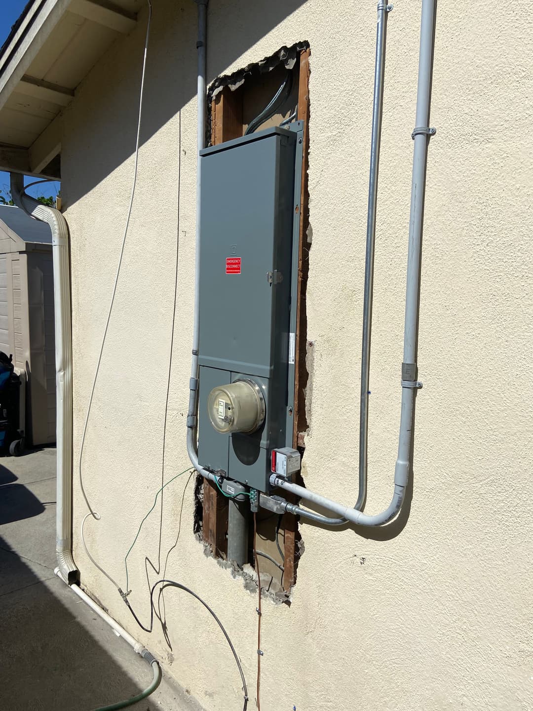 Electrical panel installation on a beige wall with exposed wiring and a gas meter.