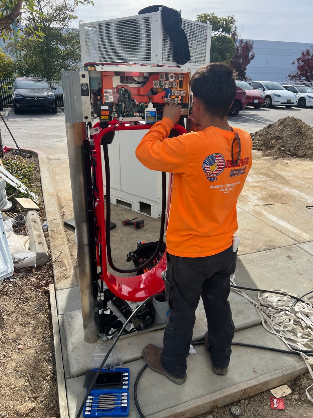 Technician repairing a charging station with tools in a structured outdoor area.