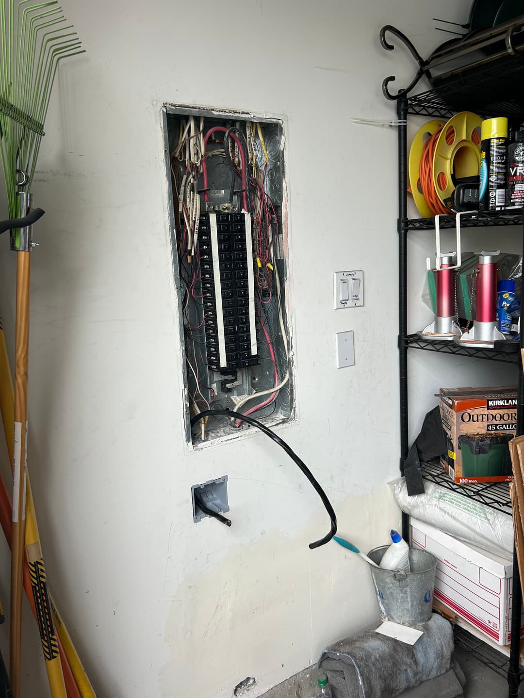 Electrical panel installed in a garage with visible wiring and nearby storage items.