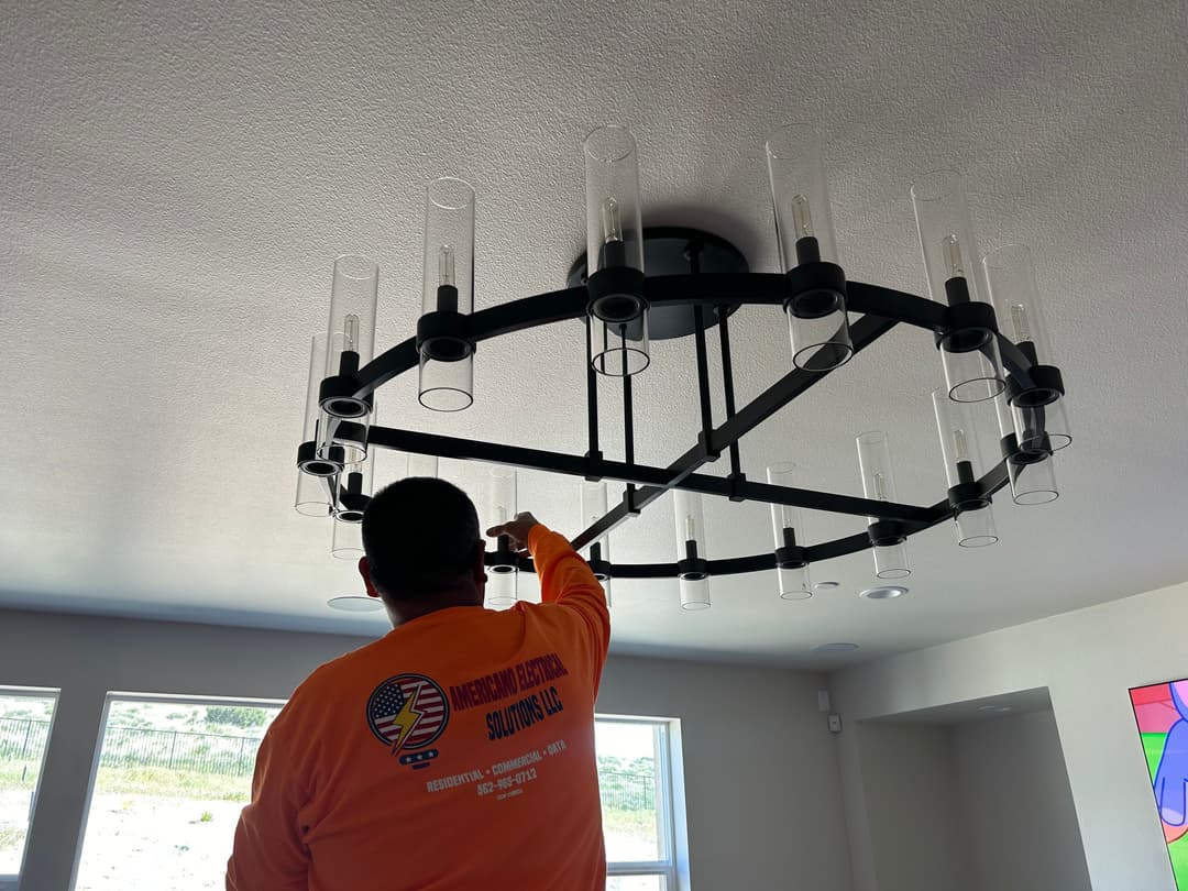 Electrician installing modern chandelier with candle-style bulbs in bright room.