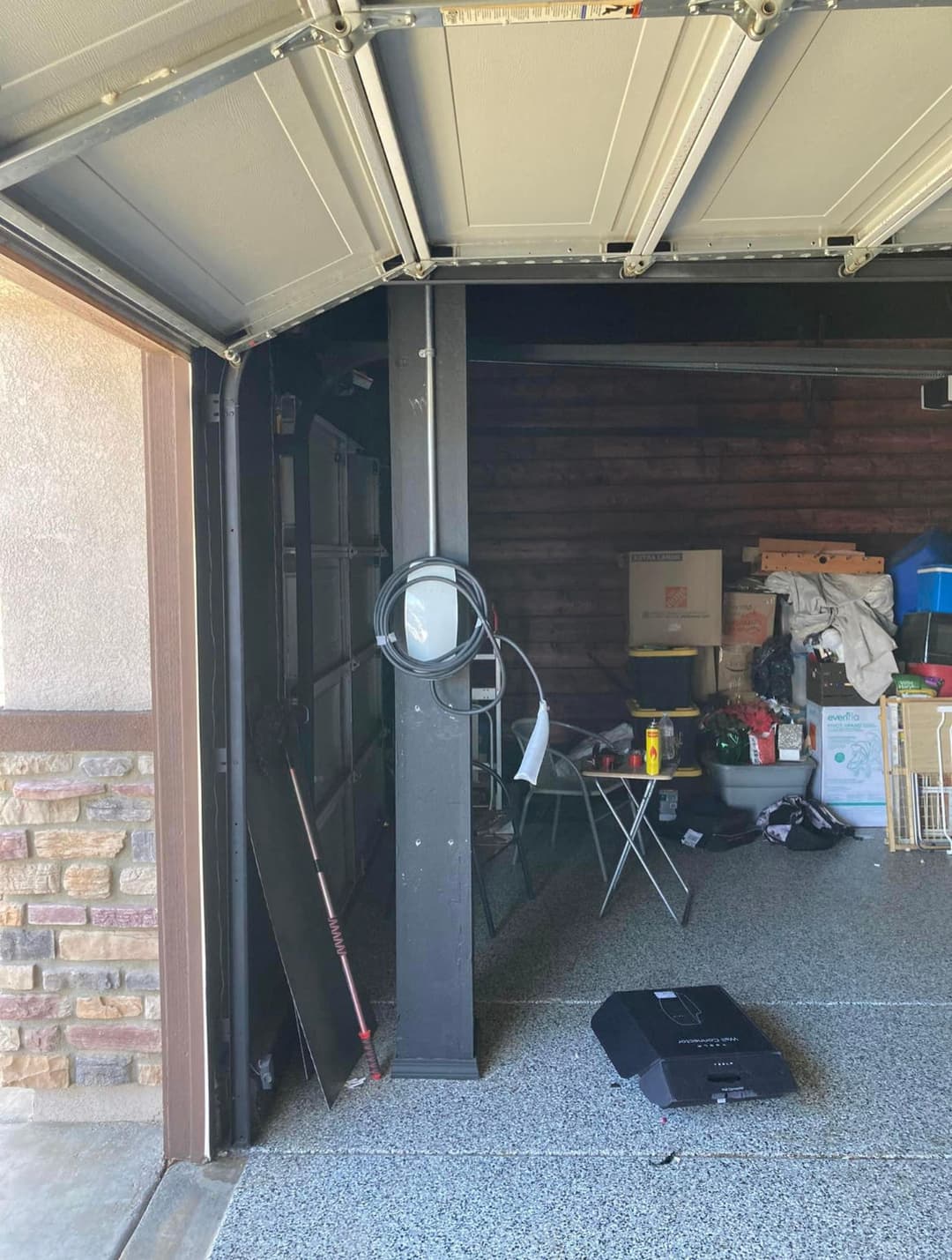 Cluttered garage interior with tools, boxes, and a folding chair beside the main door.