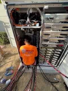 Technician working inside a large electrical cabinet with colorful cables.