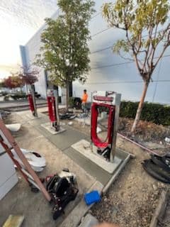 Electric vehicle charging stations under construction near a building with workers and equipment.