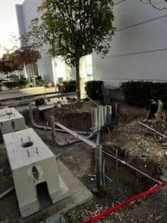 Construction site featuring underground utility work and a tree in a landscaped area.