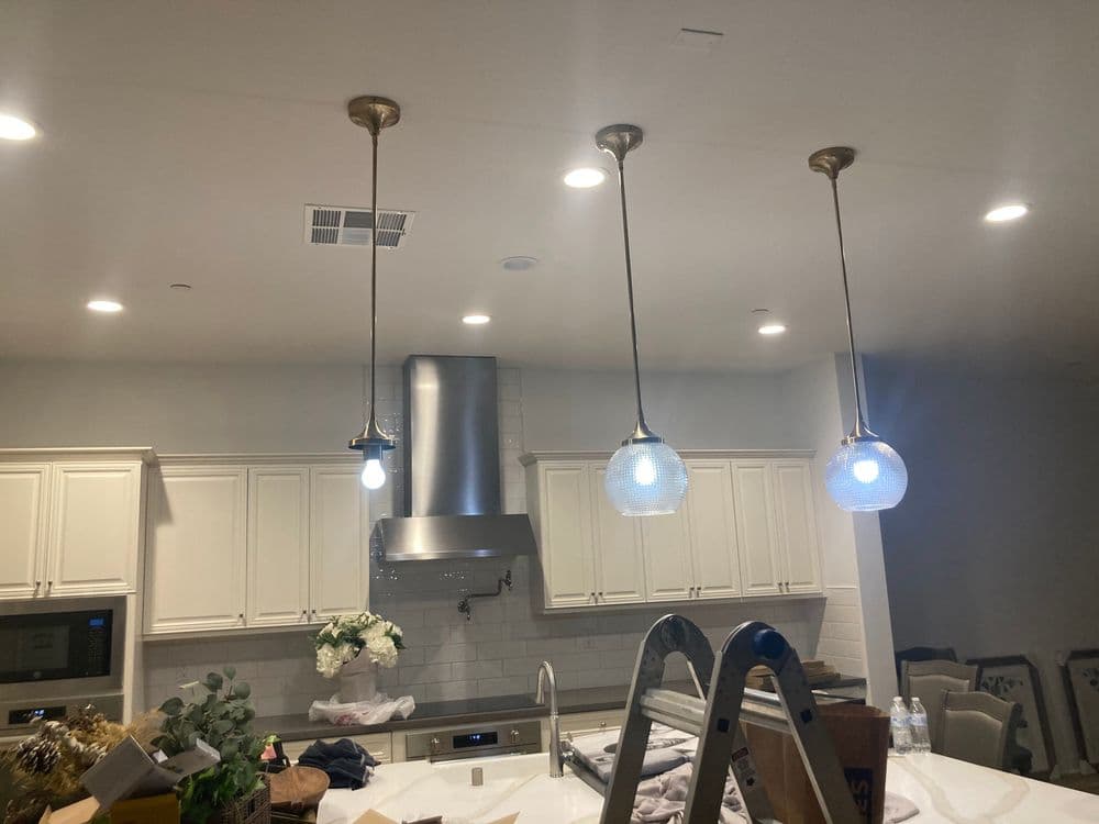Modern kitchen with three pendant lights, stainless steel range hood, and white cabinetry.