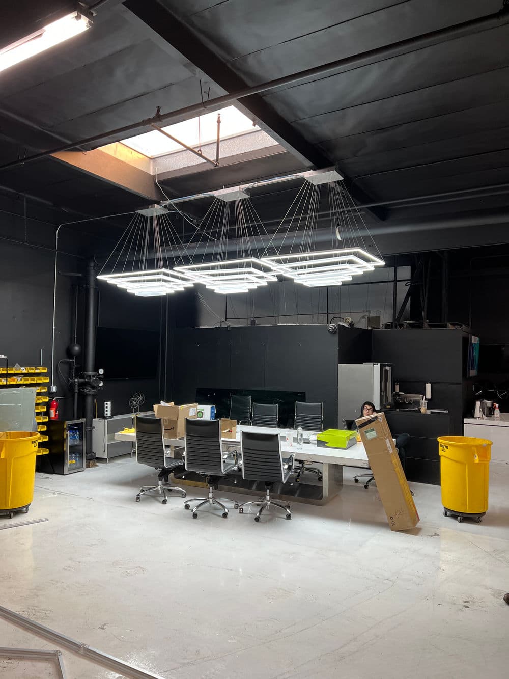 Modern office space with a large conference table, black chairs, and bright overhead lighting.